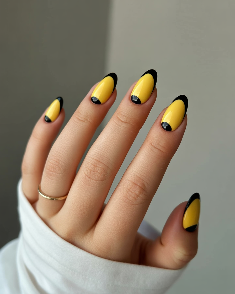 Yellow almond nails with black tips and half-moon dots.