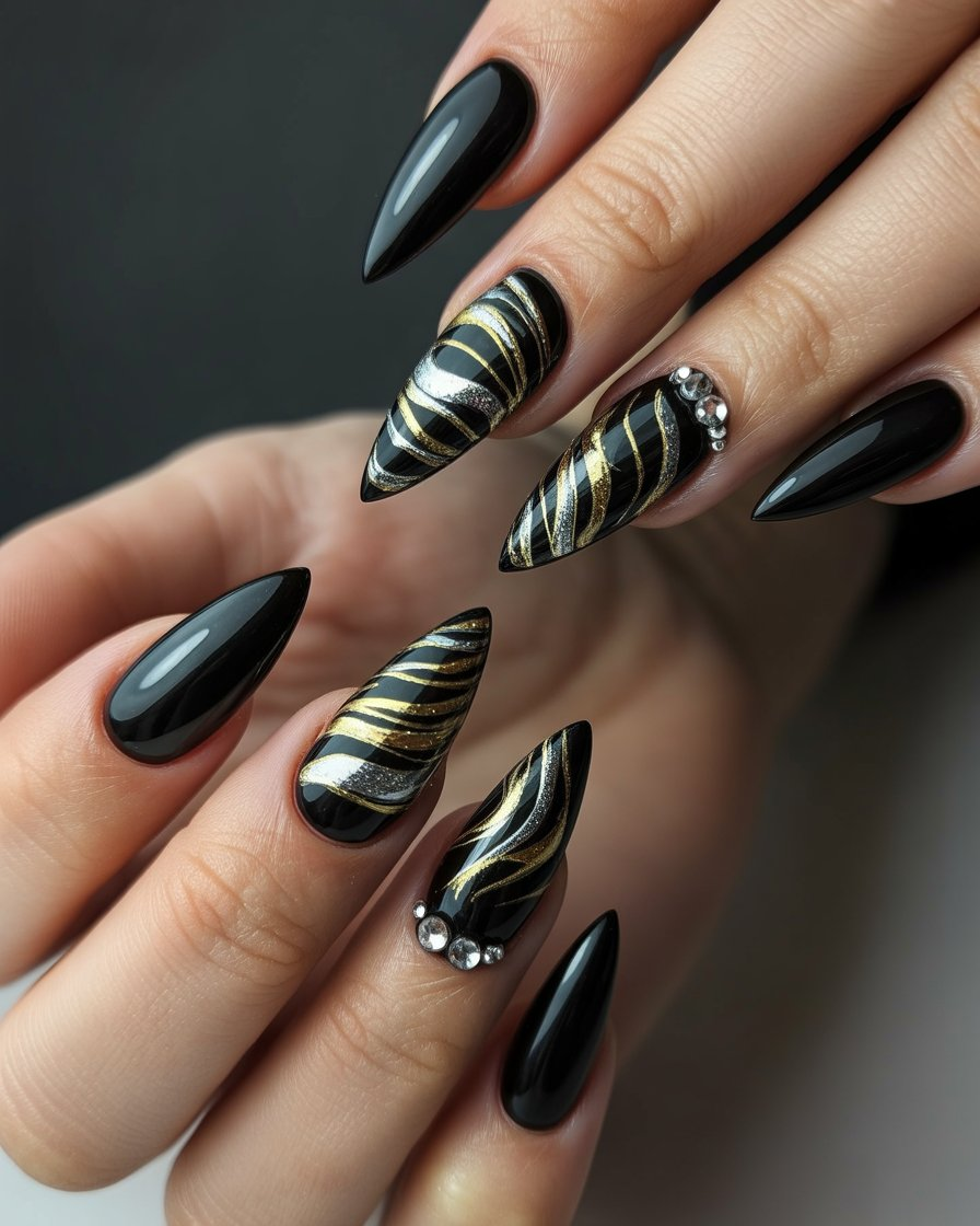 Black stiletto nails with metallic swirl designs and rhinestone accents, finished with a glossy coat for a bold and glamorous look.