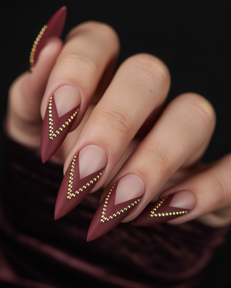 Long matte nails with deep chevron cuts and dual gold stud borders.