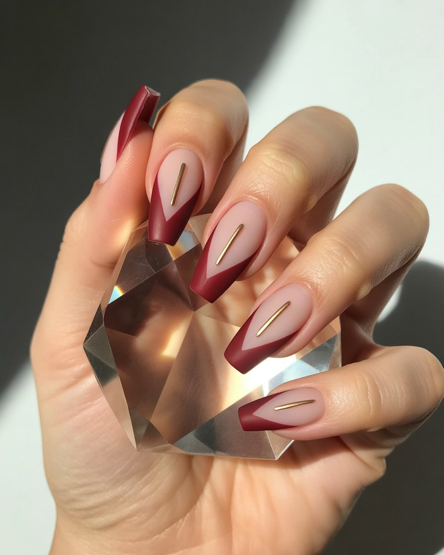 Clear base nails with burgundy chevrons and gold triangle accents.