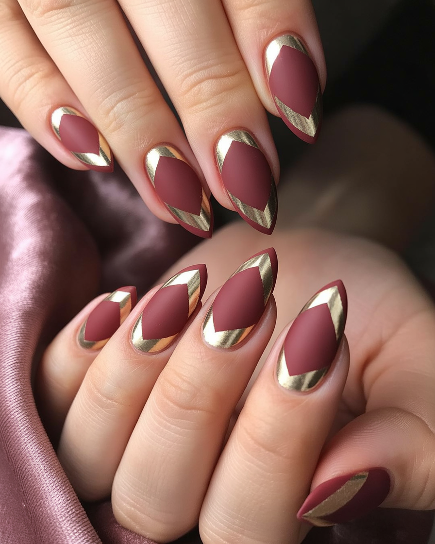  Burgundy matte nails with shiny gold foil chevron shapes.