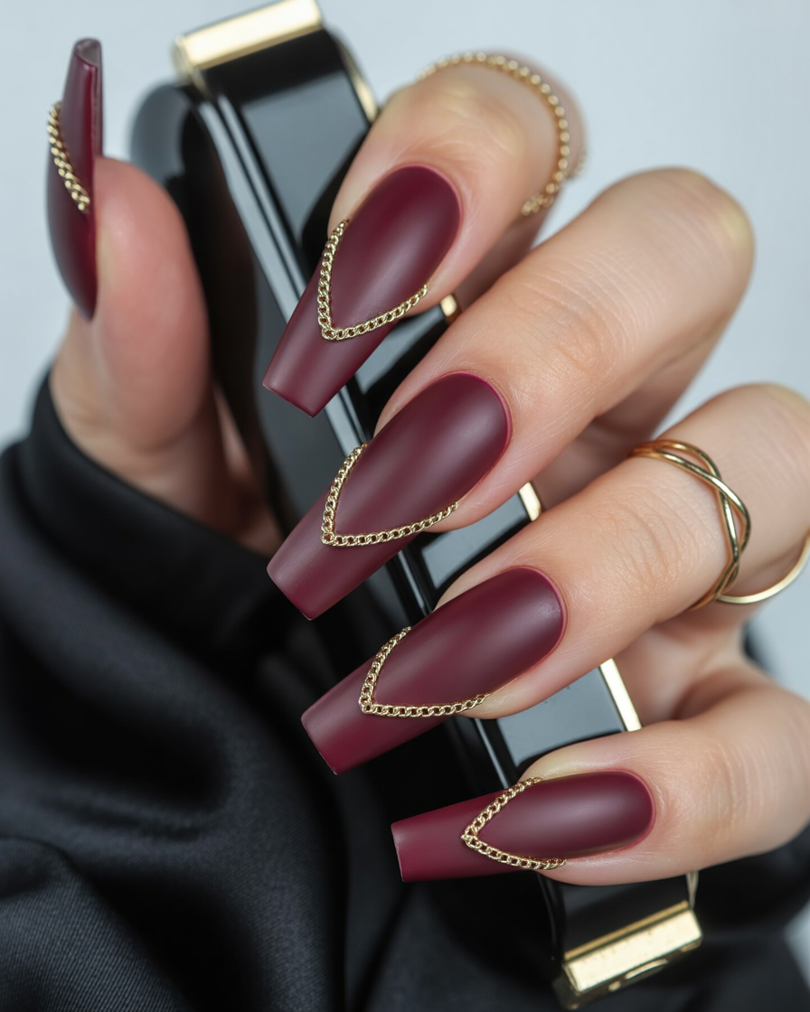  Matte burgundy nails with gold chain chevrons for a luxury finish.