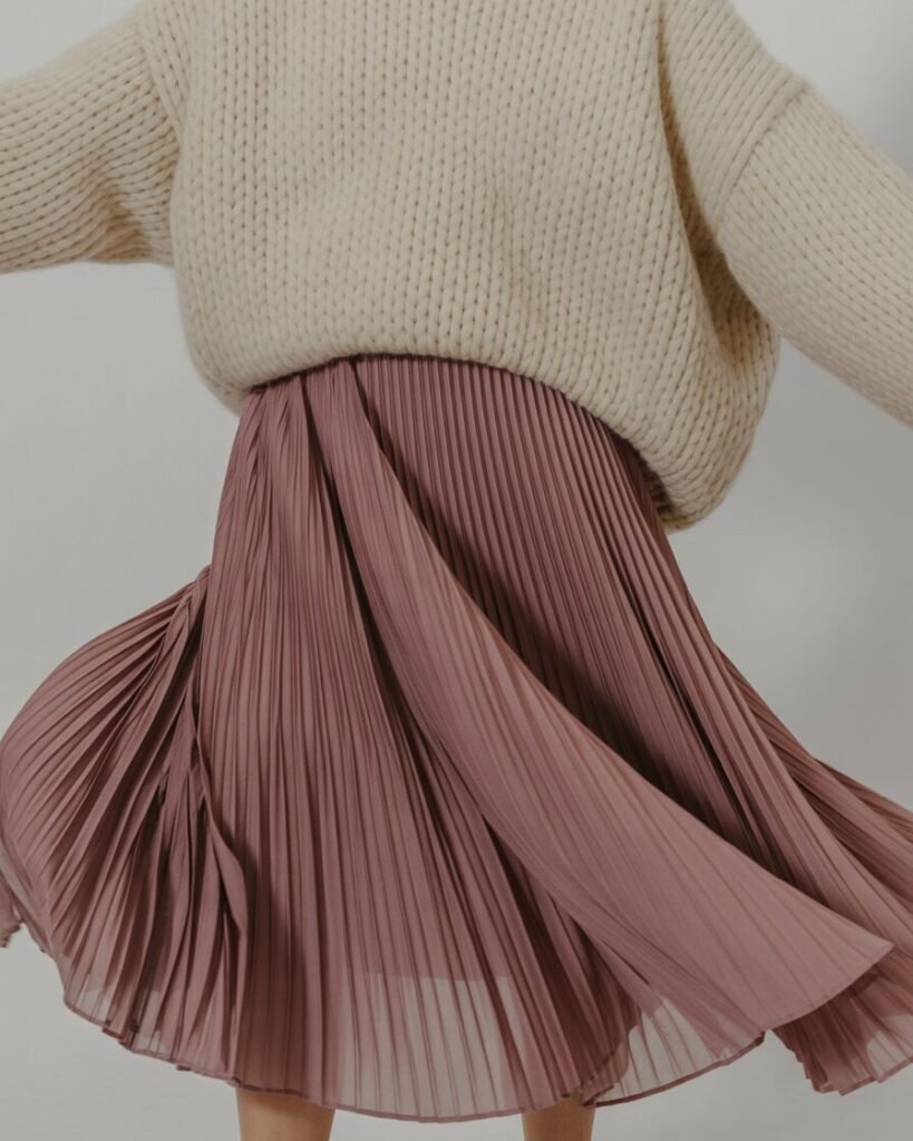 A person wearing a pleated midi skirt and a chunky knit sweater.
